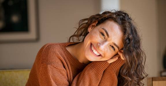 Frau mit Locken und Braunem Pulli lächelt